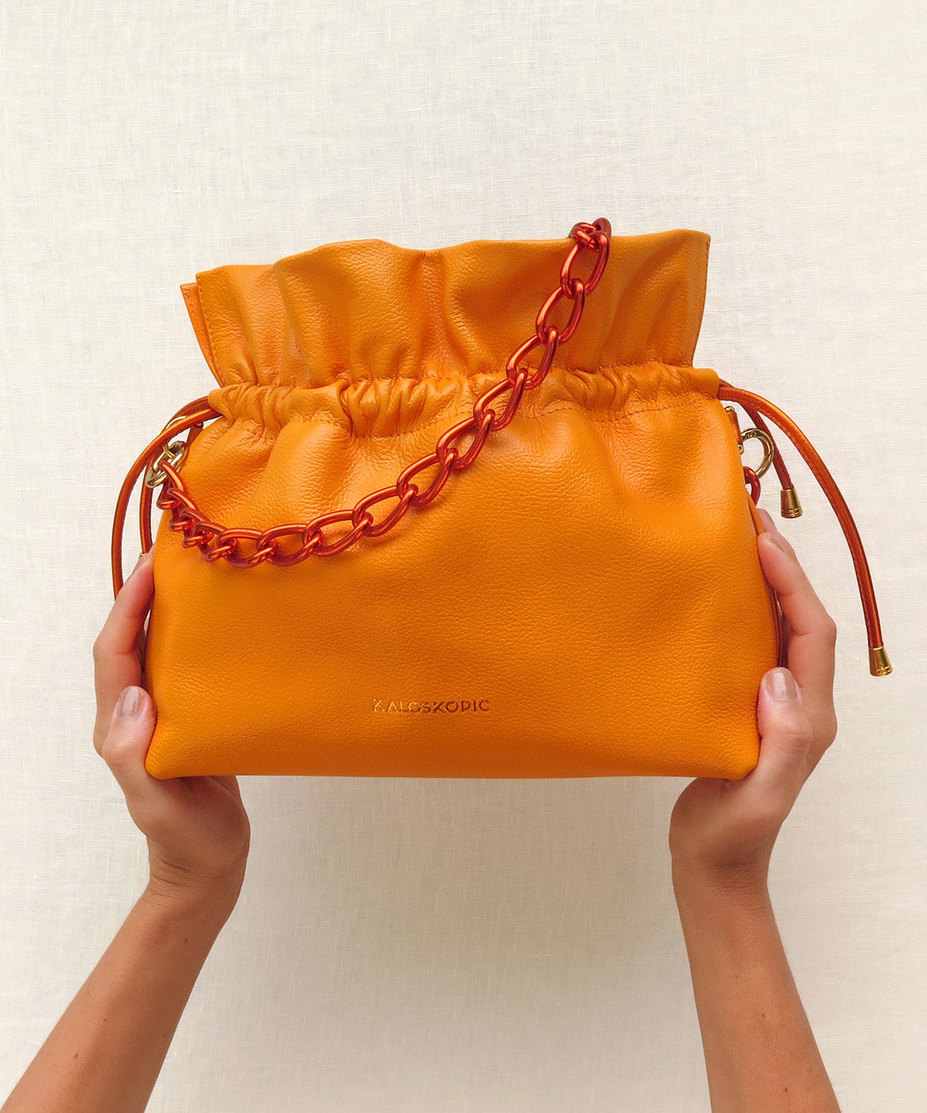 Bolso bucket cuero naranja con textura cadena corta gruesa metálica naranja Kaloskopic
